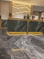 Un mostrador de recepción con encimera de mármol y diseño moderno, con una lámpara de pared y plantas en macetas.