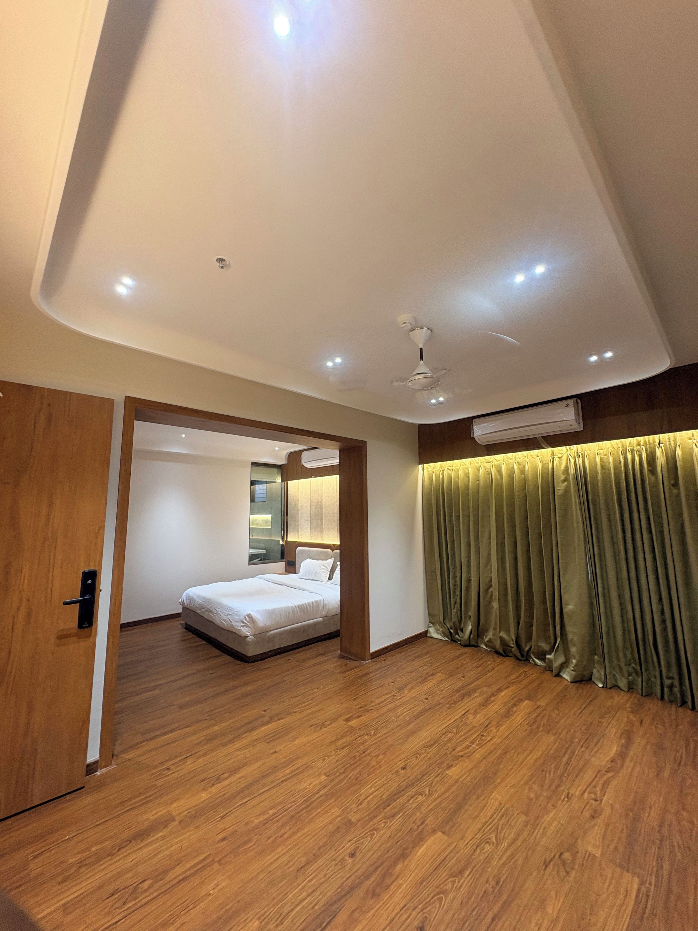 Habitación de hotel moderna con piso de madera, cama, ventilador de techo, iluminación empotrada y un ventanal grande.