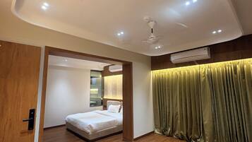 Habitación de hotel moderna con piso de madera, cama, ventilador de techo, iluminación empotrada y un ventanal grande.