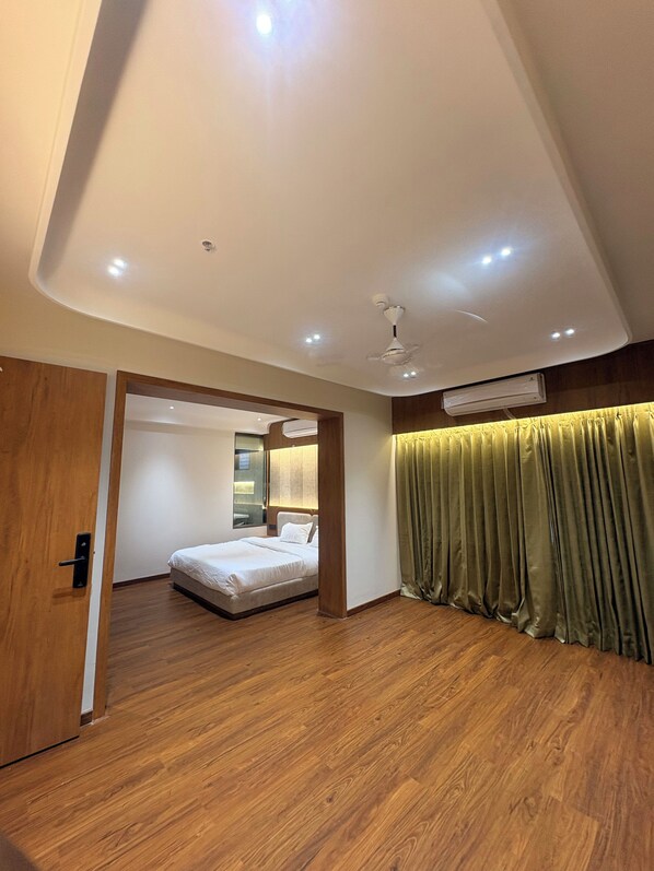 Habitación de hotel moderna con piso de madera, cama, ventilador de techo, iluminación empotrada y un ventanal grande.