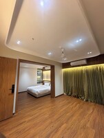 Une chambre d’hôtel moderne avec un plancher en bois, un lit, un ventilateur de plafond, un éclairage encastré et une grande fenêtre.