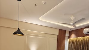A modern hotel room with a large bed, a sitting area with a chair, a bedside table, and a ceiling fan. - Majestic Park Inn (Vapi)