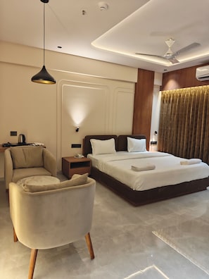 Een moderne hotelkamer met een groot bed, een zithoek met een fauteuil, een nachtkastje en een plafondventilator.