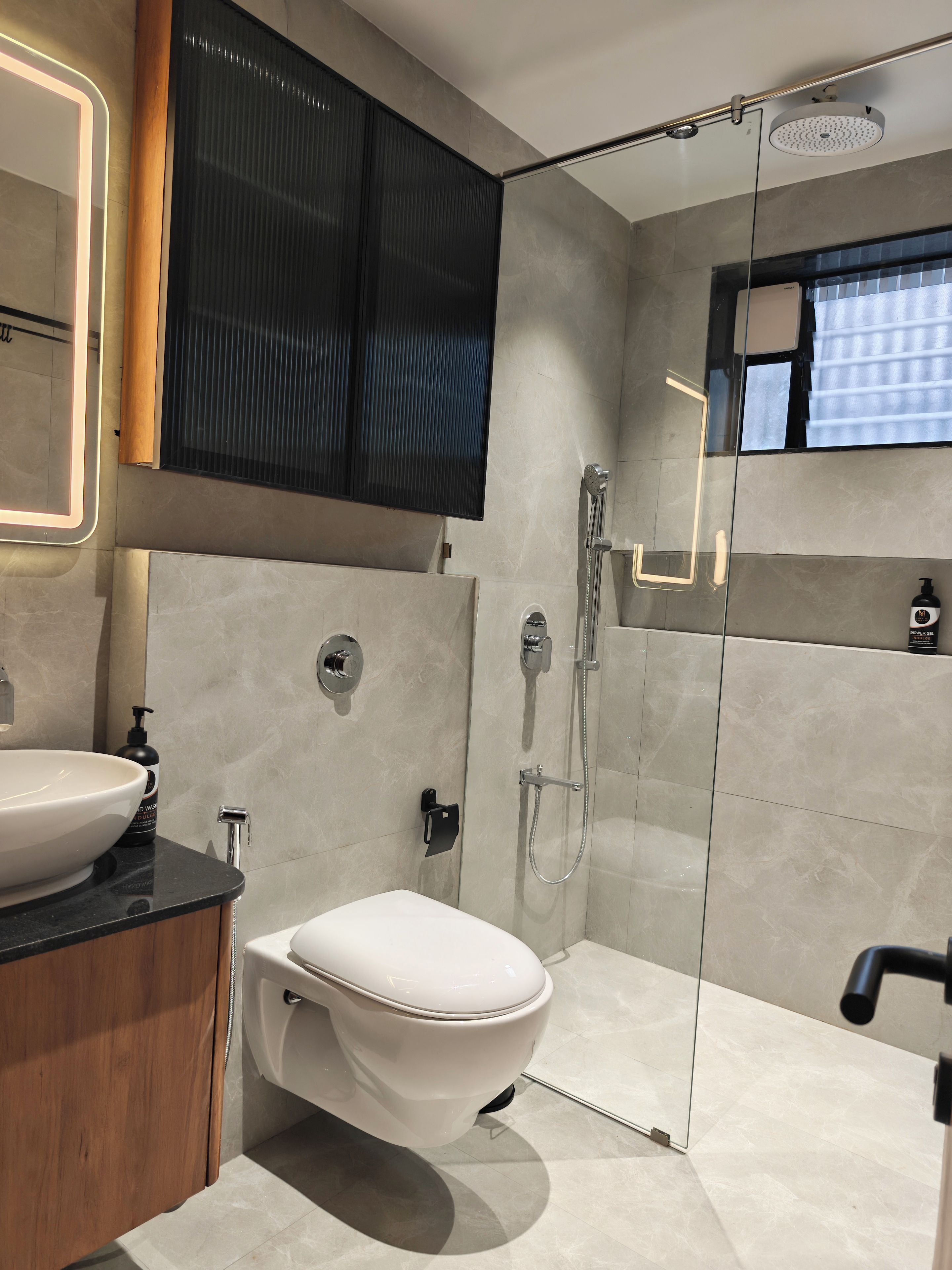 Un baño moderno con inodoro blanco, un lavabo grande, cabina de ducha y espejo con luz.