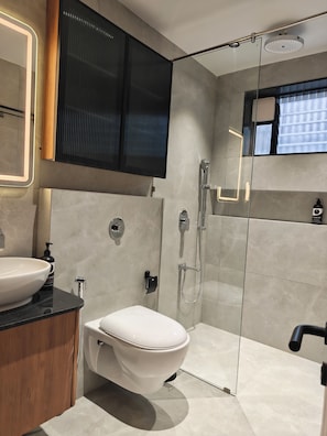 Een moderne badkamer met een wit toilet, een groot wastafelmeubel, een douchecabine en een spiegel met verlichting.