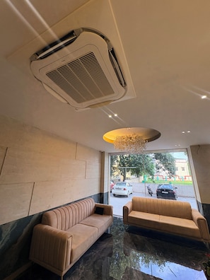 A hotel lobby with a seating area, a ceiling air vent, and a view of the street outside.