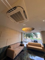 Una hall d'albergo con un'area salotto, una bocchetta di ventilazione a soffitto e vista sulla strada.