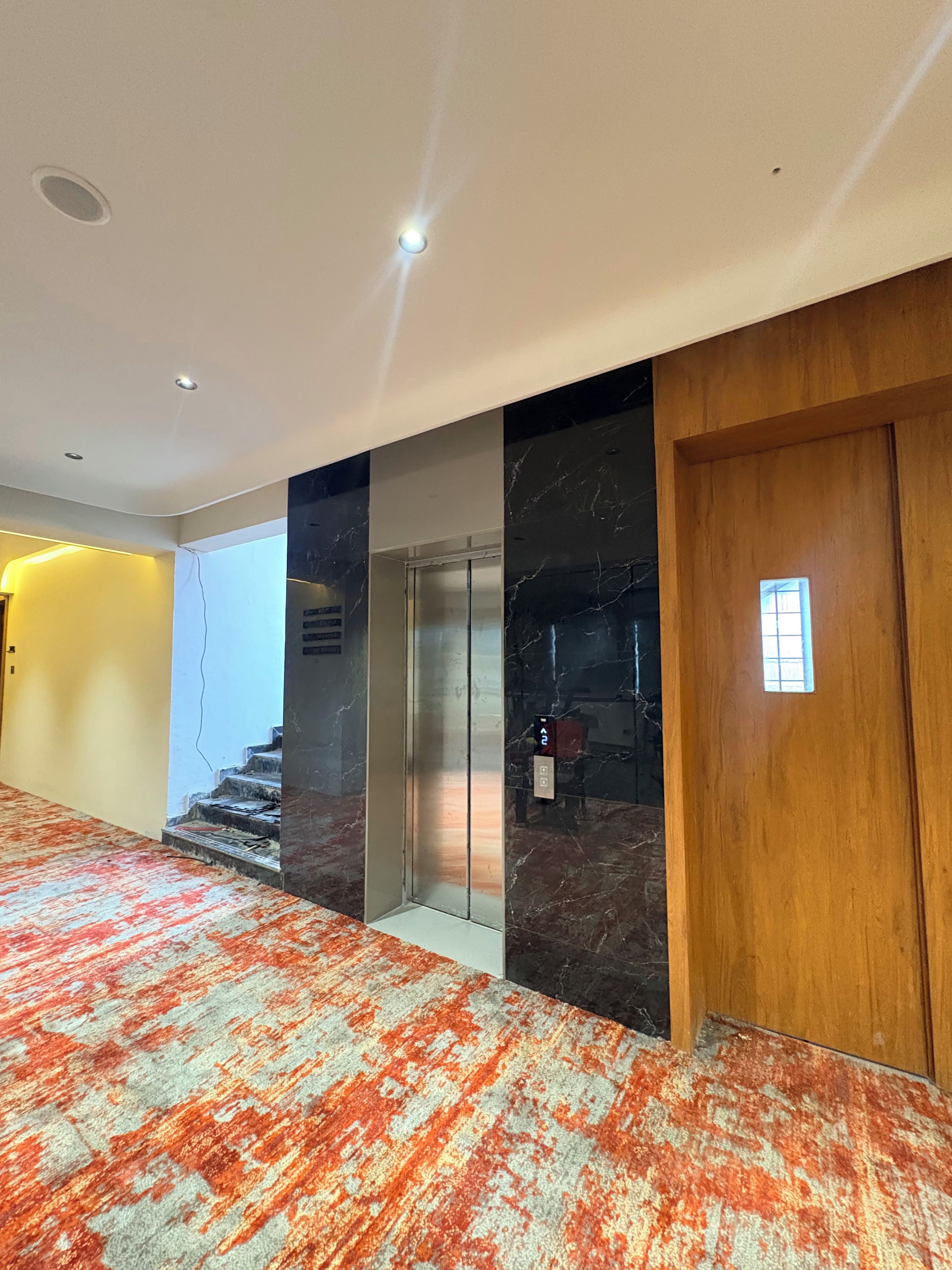 Un pasillo con piso alfombrado, una puerta de madera y una pared de mármol.
