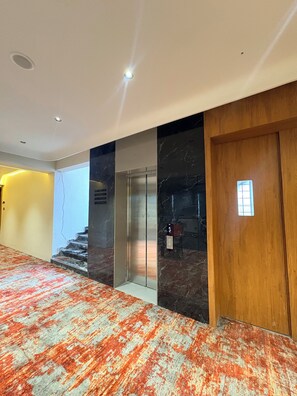 A hallway with a carpeted floor, a wooden door, and a marble wall. - Majestic Park Inn (Vapi)