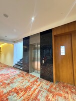 Un couloir doté d’un sol recouvert de moquette, d’une porte en bois et d’un mur en marbre.
