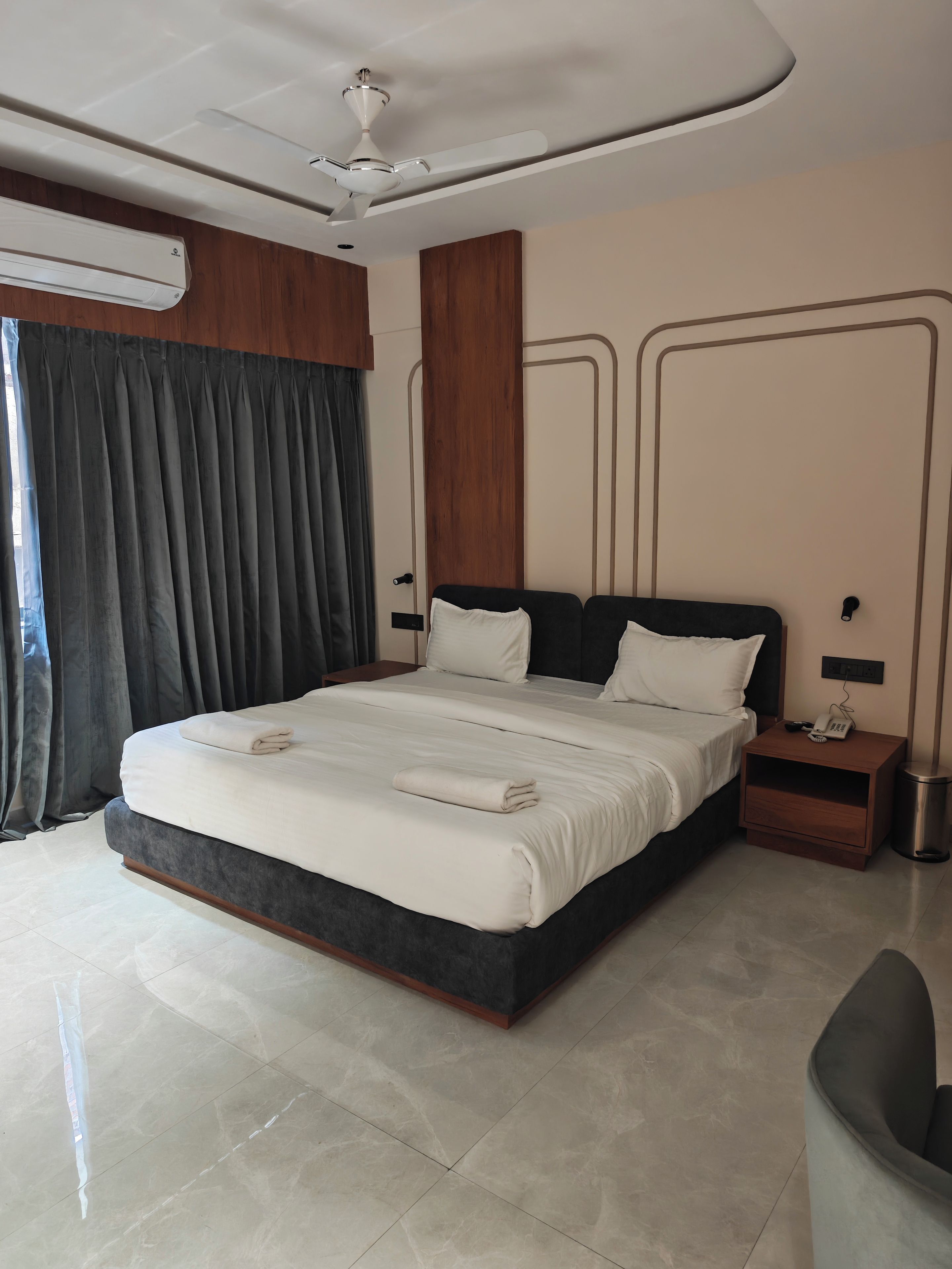 Een moderne hotelkamer met een groot bed, een nachtkastje met een telefoon, een wandairconditioner en een plafondventilator.