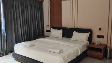 A modern hotel room with a large bed, a bedside table with a phone, a wall-mounted air conditioning unit, and a ceiling fan.