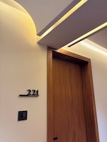 A hotel room with a wooden door, a number sign, and a light switch.