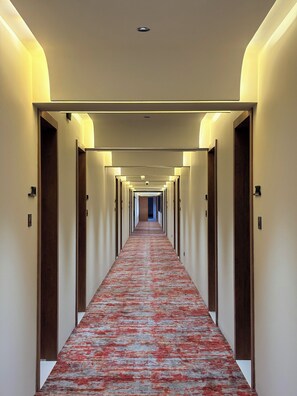 A hotel hallway with a carpeted floor, doors on both sides, and overhead lighting.