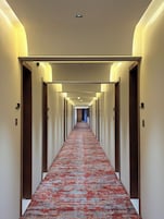 A hotel hallway with a carpeted floor, doors on both sides, and overhead lighting.
