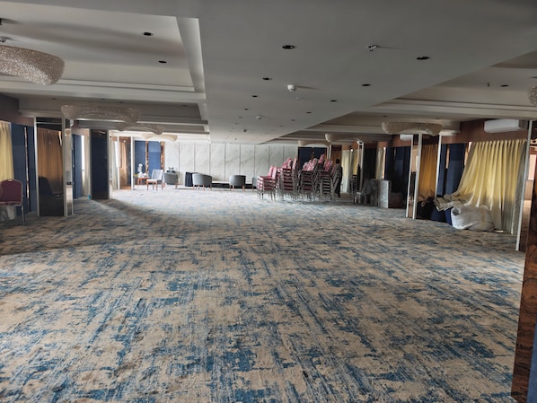 A spacious hall with a patterned carpet, rows of chairs, and a high ceiling with recessed lighting.