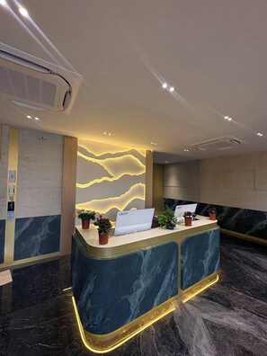 A reception desk with a laptop, potted plants, and a wall with a wave-like design.