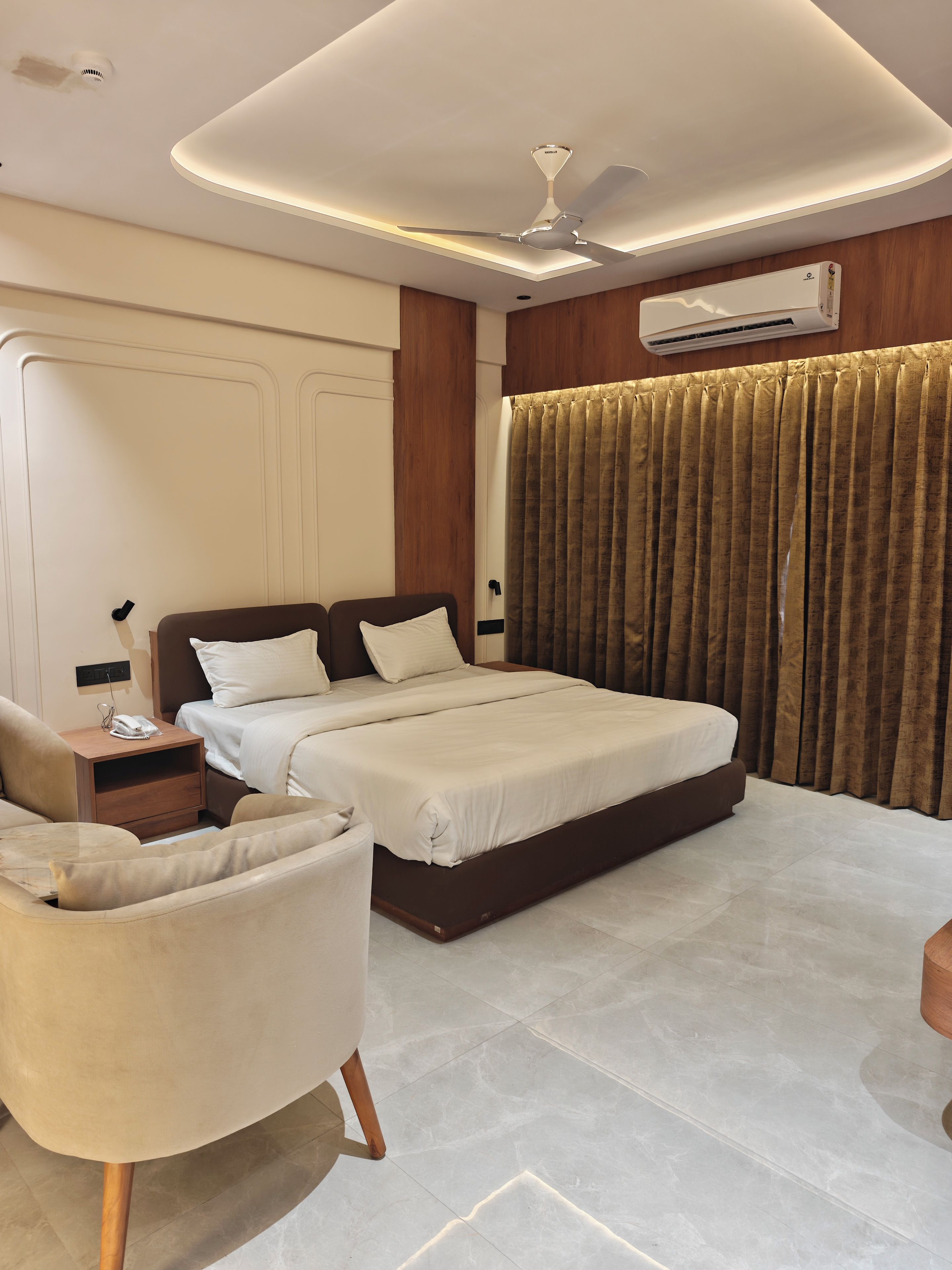 A modern hotel room with a large bed, a bedside table, a chair, and a ceiling fan.