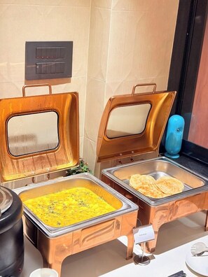 Un buffet avec deux distributeurs de nourriture ouverts : l’un contient un plat jaune et l’autre, des pains plats.