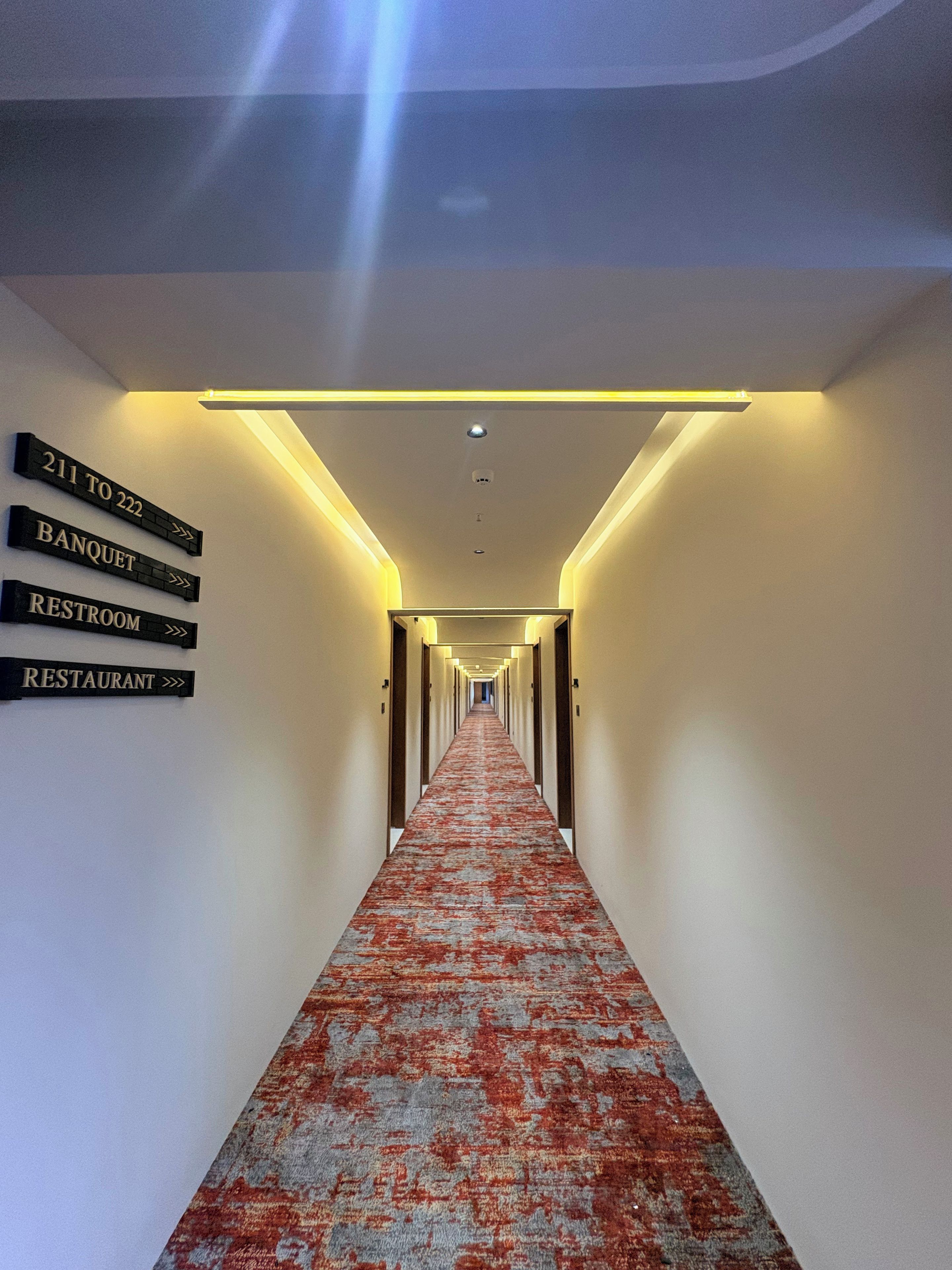 Un corridoio d'hotel con segnali direzionali per le camere 211-222, una sala ricevimenti, un bagno e un ristorante.