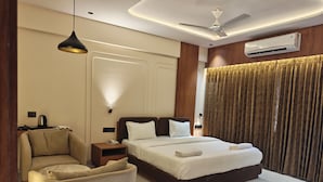 A hotel room with a bed, a chair, a bedside table with a lamp, an air conditioning unit, and a ceiling fan. - Majestic Park Inn (Vapi)
