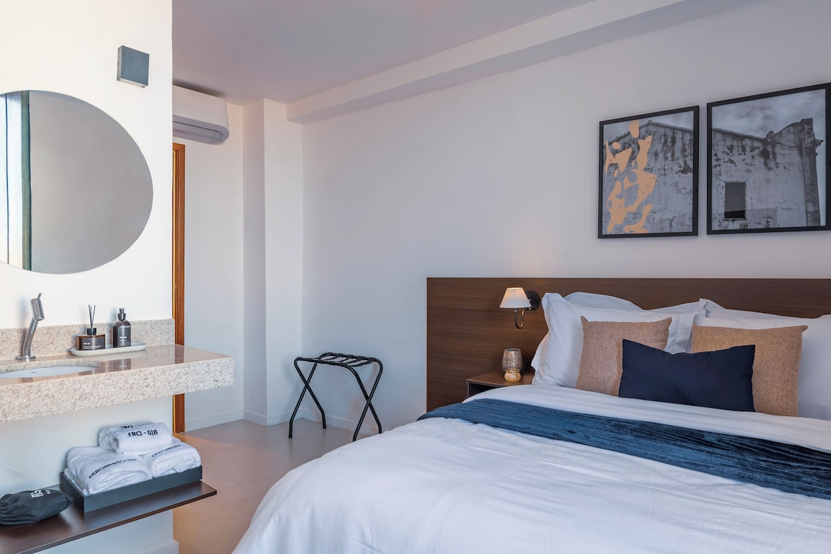Ein modernes Hotelzimmer mit einem großen Bett, einem Badezimmerwaschtisch und zwei gerahmten Bildern an der Wand.