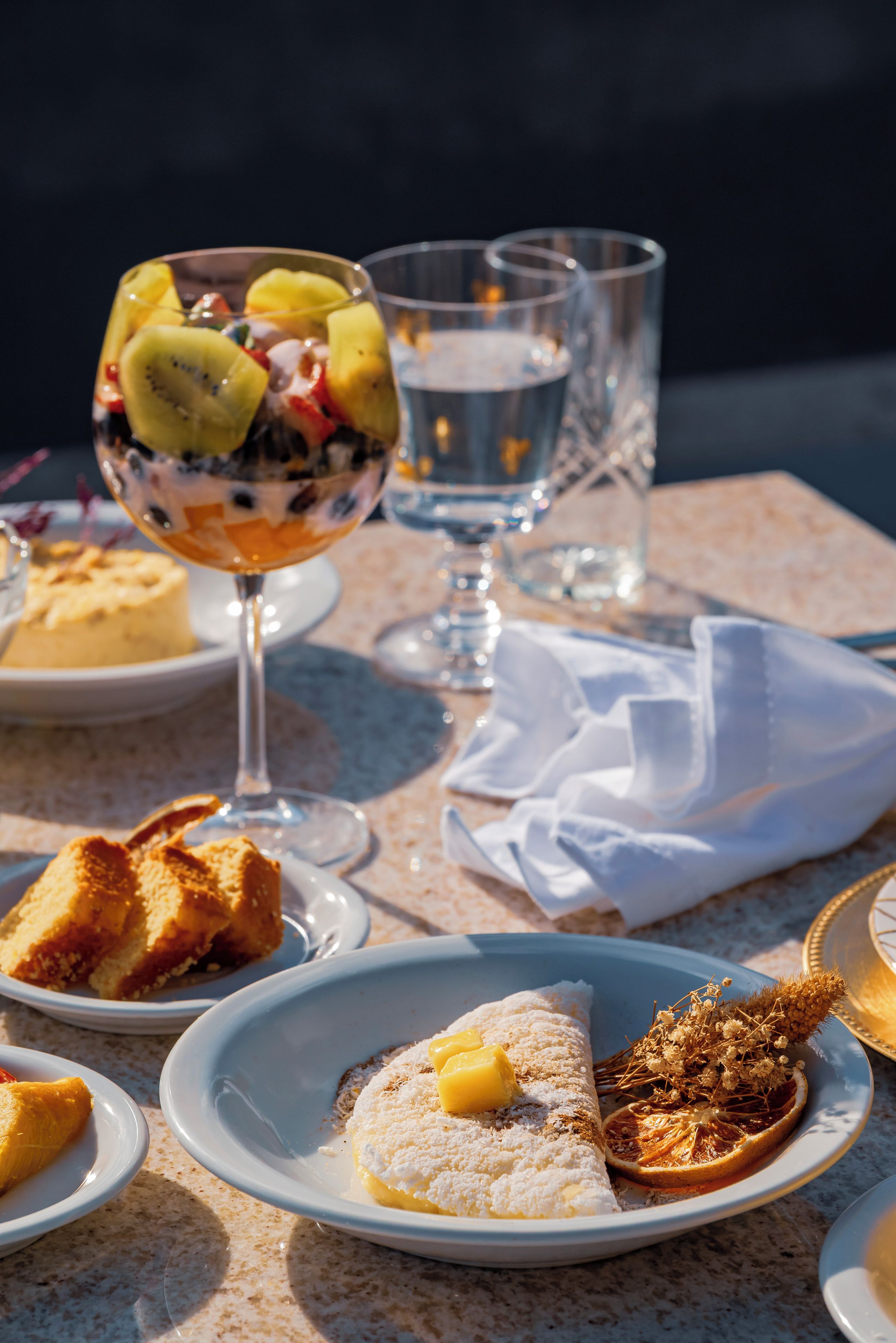 Una mesa dispuesta con varios platos, incluyendo un postre de fruta en un vaso, un plato con un pastel y un vaso de agua.