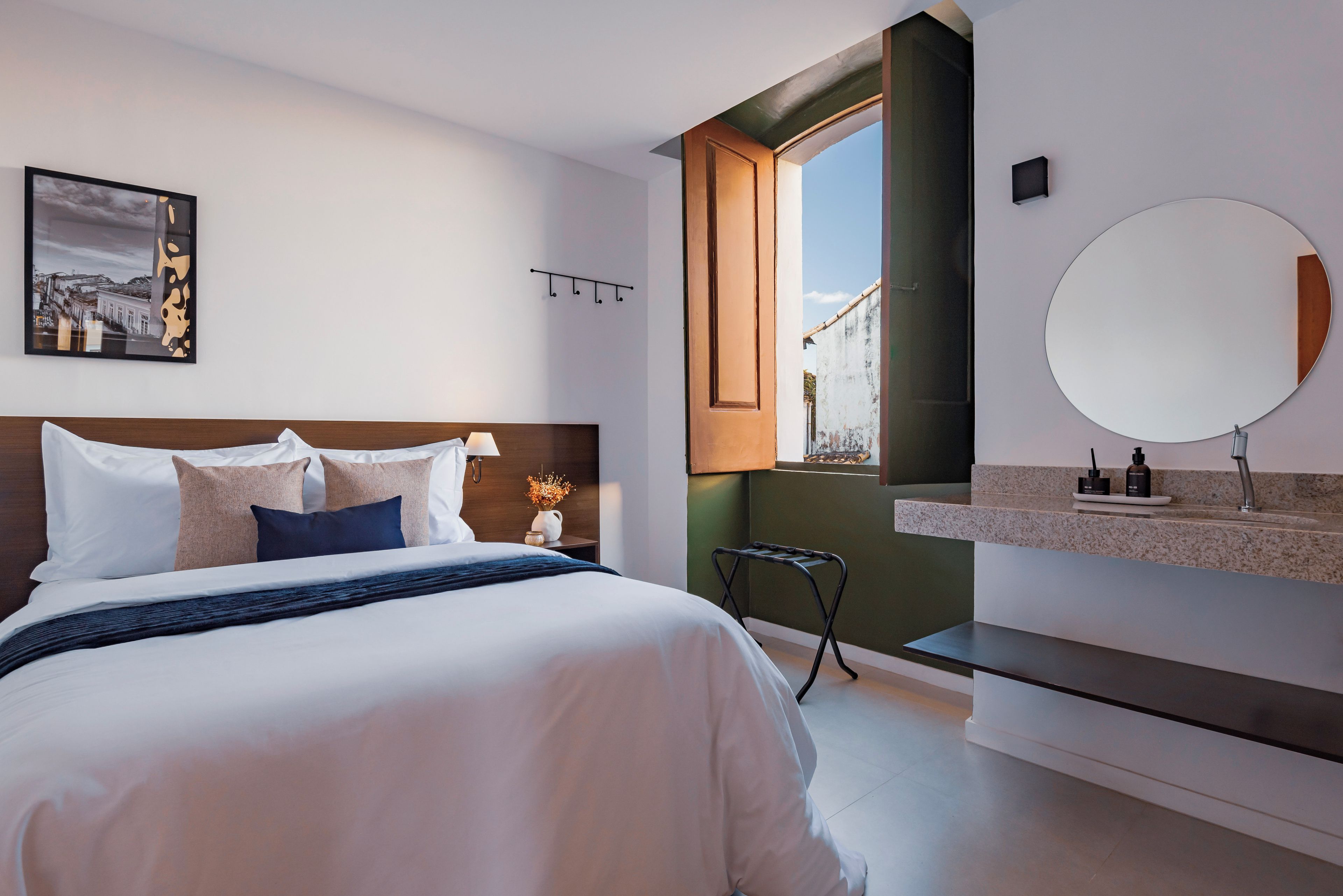A modern bedroom with a bed, bedside table, lamp, and a view of the outside.
