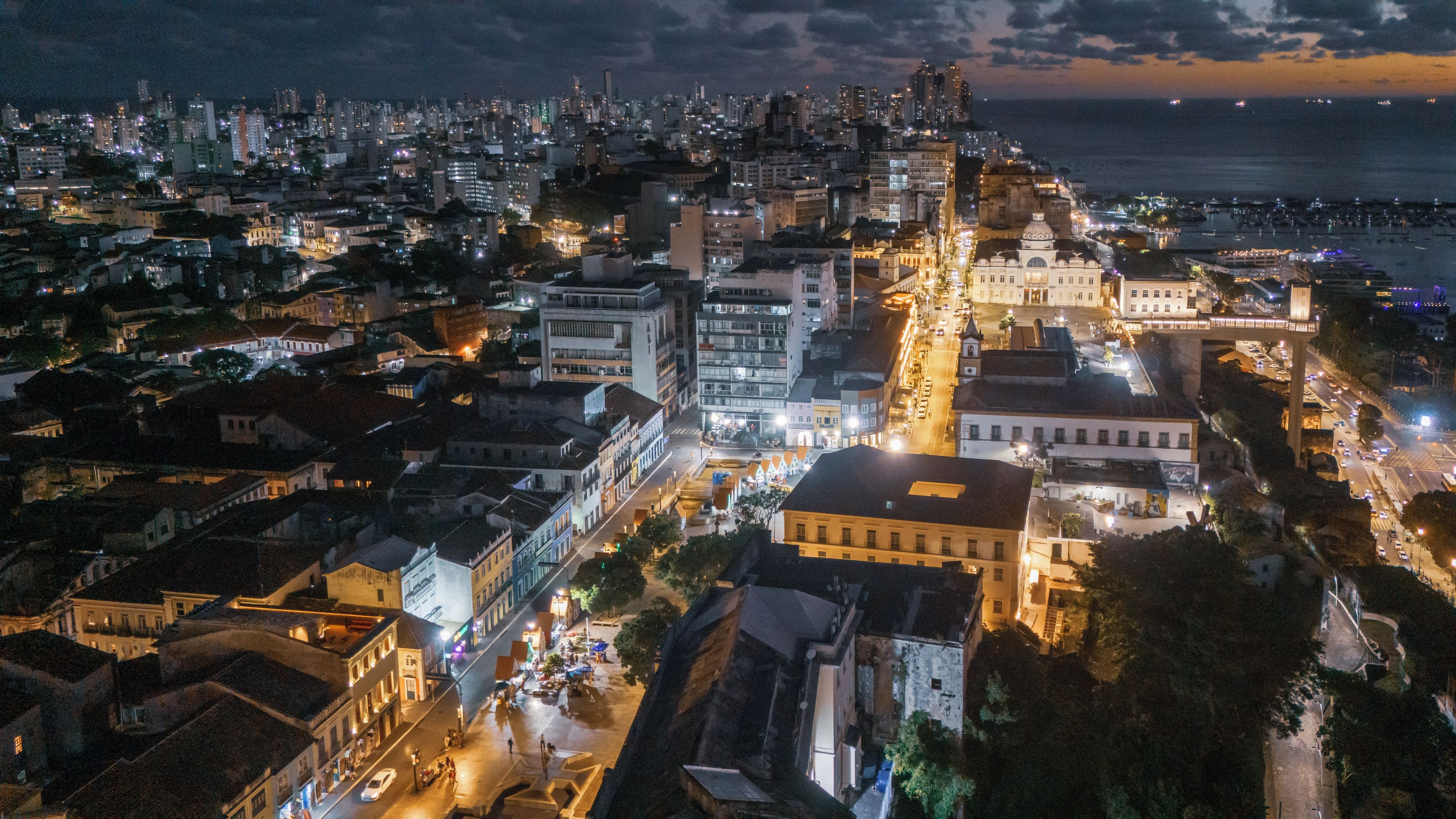 A nighttime cityscape with illuminated buildings and a view of the sea.