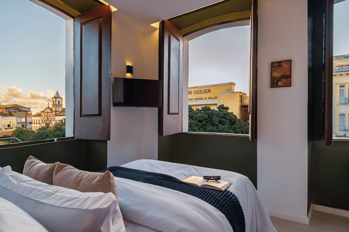 Ein Hotelzimmer mit Bett, Fenster mit Stadtblick, einem Wandfernseher und einem Bild an der Wand.