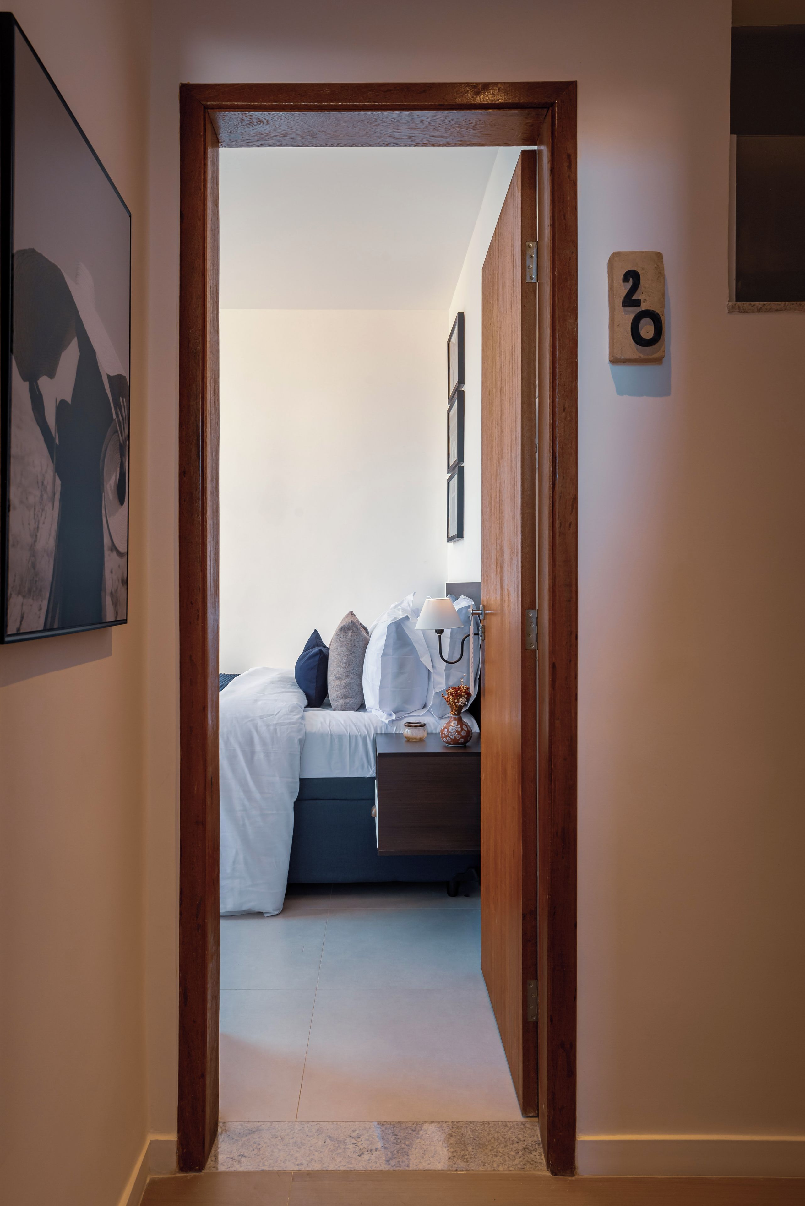 Una puerta que da a un dormitorio con cama, almohadas, una mesita de noche y un florero.