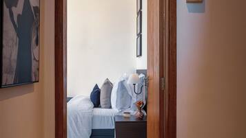 Una puerta que da a un dormitorio con cama, almohadas, una mesita de noche y un florero.