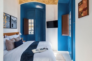 Ein Schlafzimmer mit einem großen Bett, einem flachbildfernseher an der Wand und einem Fenster mit Blick ins Freie.