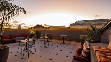 En takterrass med ett område för måltider, sittplatser och utsikt över stadsbilden vid solnedgången.
