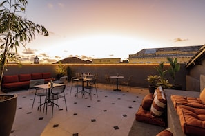 Una terraza en la azotea con zona de comedor, asientos y vistas a la ciudad al atardecer.
