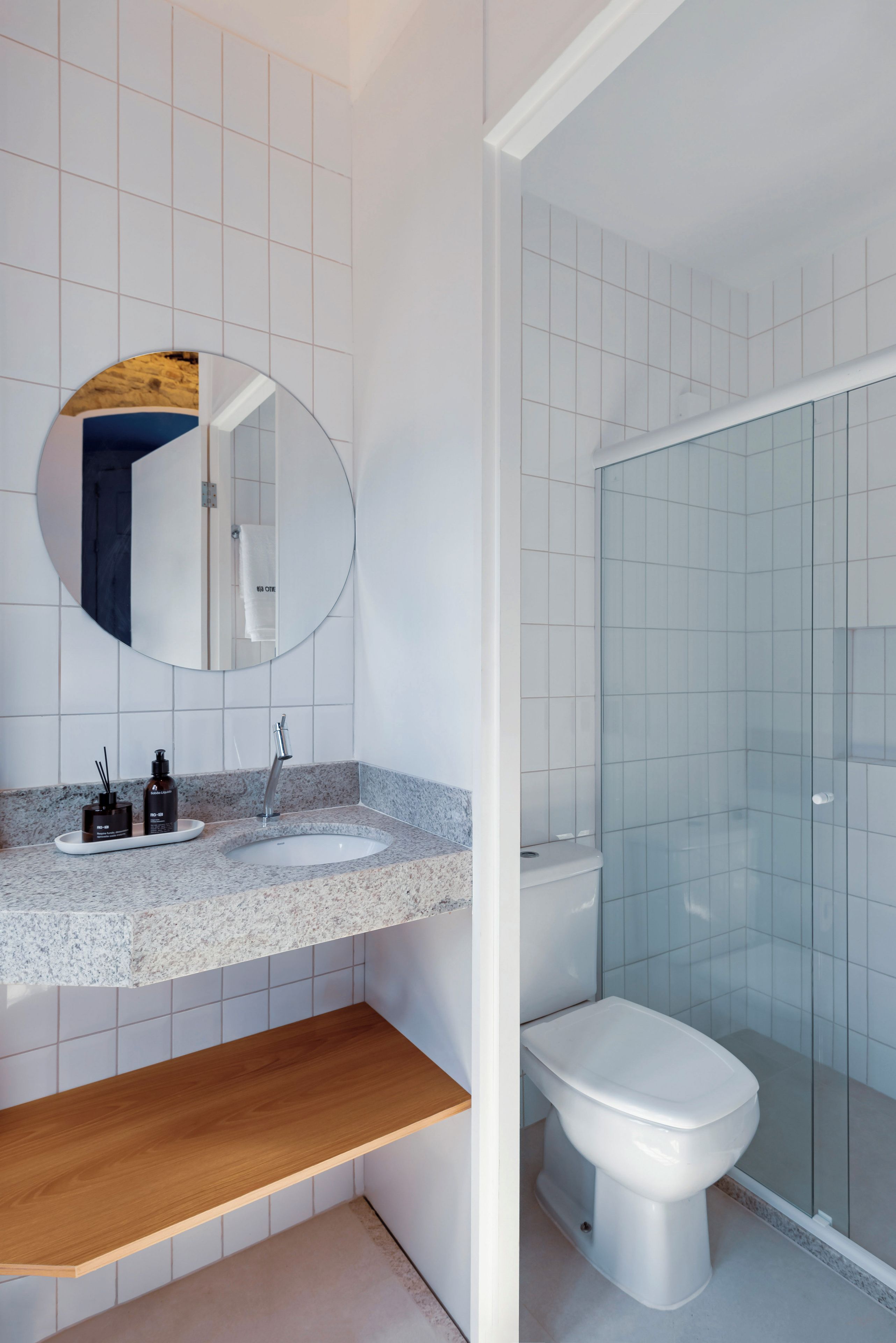 Un baño moderno con un espejo redondo, un lavabo con dos botellas, un inodoro y una cabina de ducha de vidrio.
