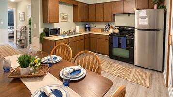 A modern kitchen with wooden cabinets, a stainless steel refrigerator, and a dining area set with blue plates and a vase of flowers.
