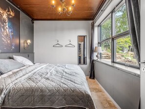 Een slaapkamer met een groot bed, een kroonluchter, een kledingkast en een raam met uitzicht op bomen.