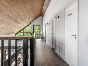 Een gang met een houten plafond, witte muren en een deur met een greep.