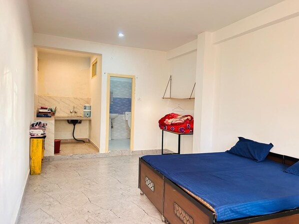 A bedroom with a bed, a small table, a chair, and a bathroom visible through an open door.