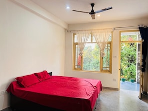 A bedroom with a bed, a ceiling fan, a window with sheer curtains, and a view of greenery outside.