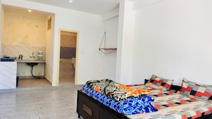 A bedroom with a bed, a bedside table, a hanging light fixture, and a bathroom visible through an open door.
