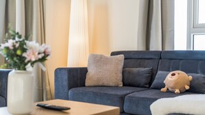 Ein modernes Wohnzimmer mit einem dunkelblauen Sofa, einem beigen Kissen, einem Stofftier, einer Vase mit Blumen und einer Fernbedienung auf einem Holztisch.