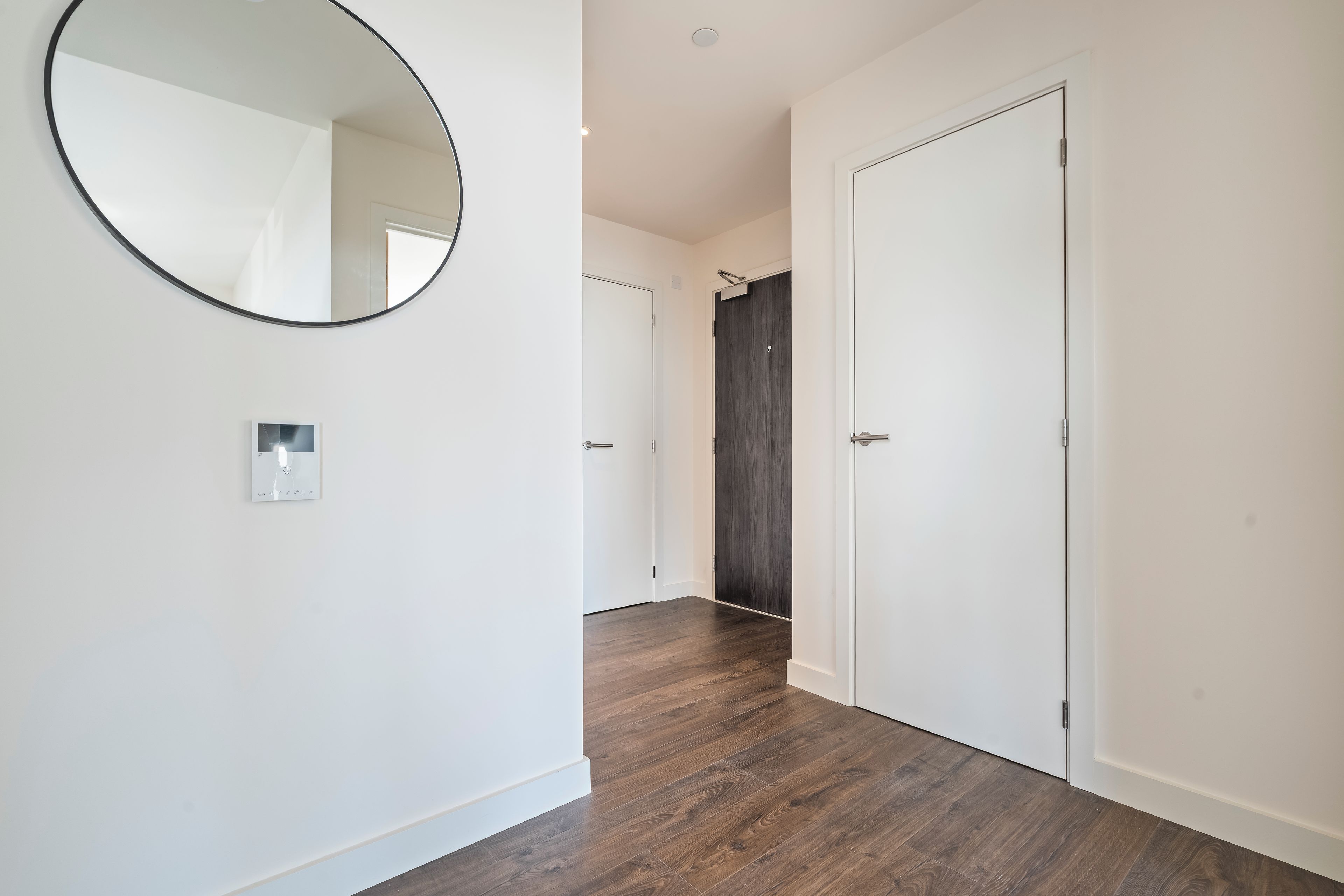 A hallway with a round mirror, a light switch, and a door with a dark wood finish.