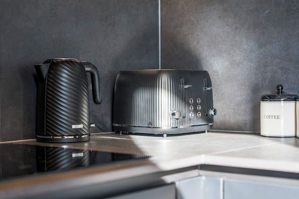 Et køkken med kaffemaskine, elkedel og brødrister på en bordplade.