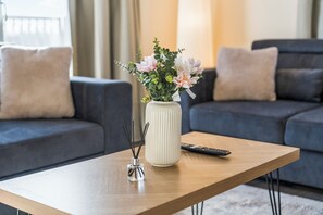 Un salon moderne avec une table basse en bois, un vase rempli de fleurs, une télécommande et un porte-bougie décoratif.
