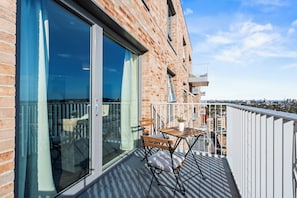 En balkon med et bord og stole, en potteplante og udsigt over bybilledet.