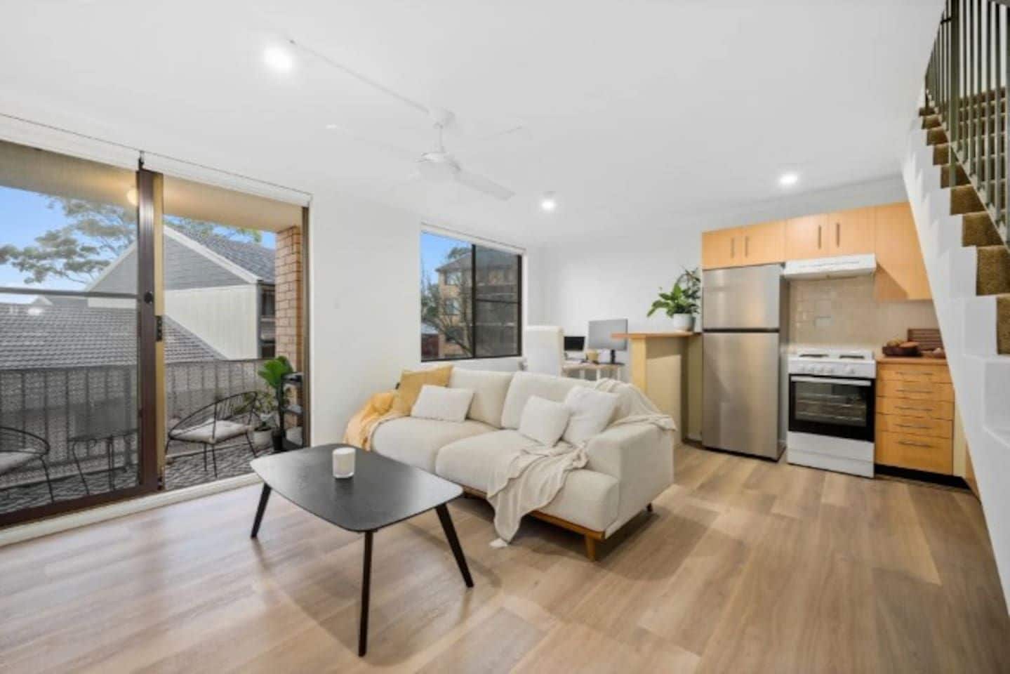 A modern apartment with a living area, kitchen, and a staircase.