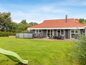 Ein modernes Haus mit rotem Ziegeldach, einer überdachten Terrasse mit Gartenmöbeln und einem grünen Rasen.