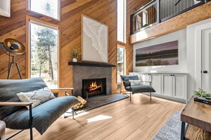 A cozy living room with a fireplace, wooden floors, and a view of the outdoors. - Cozy Sunriver Fall Escape+3BR Family Getaway+Sleeps 8+Wood Burning Fireplace (Sunriver)